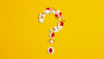 Red and white pills, tablets and other medications arranged in a question mark shape on a yellow background.
