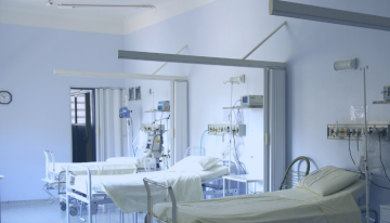 Empty hospital beds in a white room, with medical equipment. Used to illustrate how design influences healthcare in hospitals.